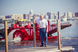 Joe Yaeger surveys the boat launch at Olin Park while a weed harvester passes by on Lake Monona.