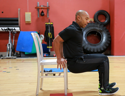 Fitness trainer Jesse Sherman of Harbor Athletic Club demonstrates the proper way to do squats at your office chair. Most people do exercises the wrong way, he says, causing knee and back pain in the case of squats, and tension in the shoulders instead of “feeling it” in the chest in the case of pushups.