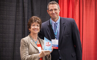Kristine Ashe shows off her Fittest Executive Challenge trophy next to IB Publisher Jon Konarske.