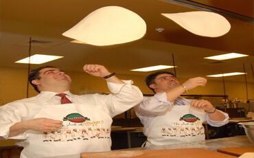 Giacomo Fallucca president and CEO of Palermo’s Pizza, left, tosses a pizza with brother Angelo, the company’s COO.