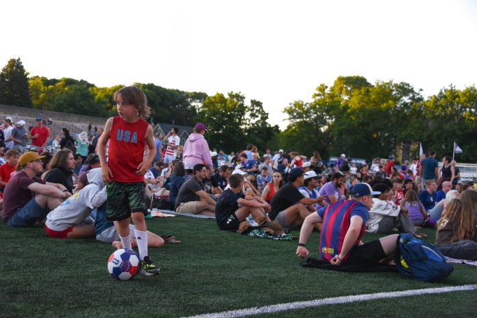 A boy to the left of the image dribbles a football while fans in the background fill Breese Stevens for the June 12 USA opener versus Paraguay at the 2026 World Cup.