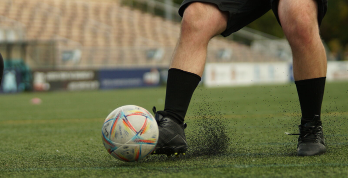 A man dribbles a soccer ball across a turf field.
