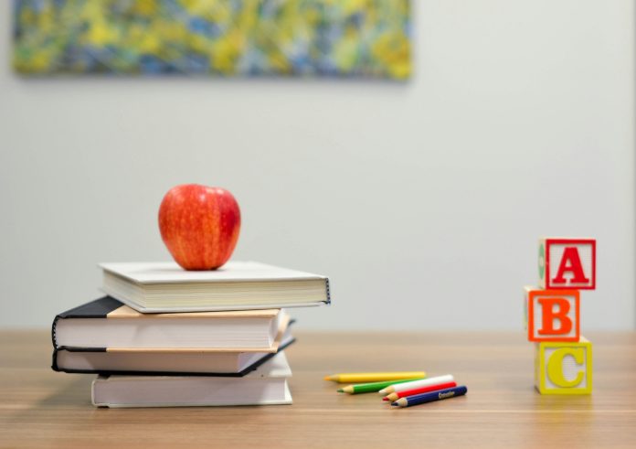 Books stacked on top of each other with an apple on top. A, B, and C blocks stacked to the right of the books on a school desk.