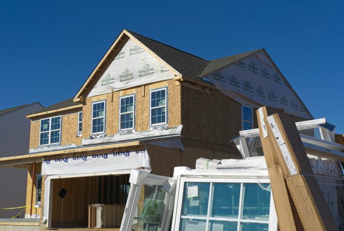 A home being built, with wood and insulation shown, as well as windows set on the ground waiting to be installed.