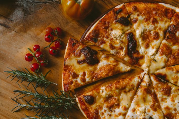 Cheese pizza next to a tomato on a wood table.