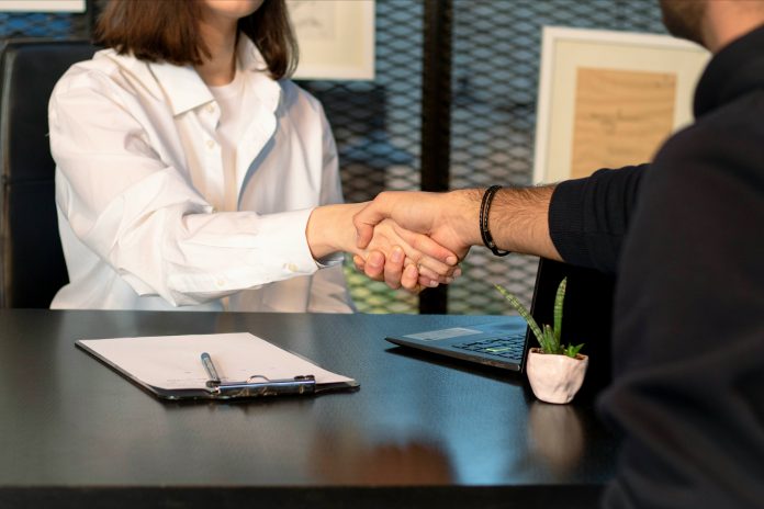 A man and woman shake hands over a desk.