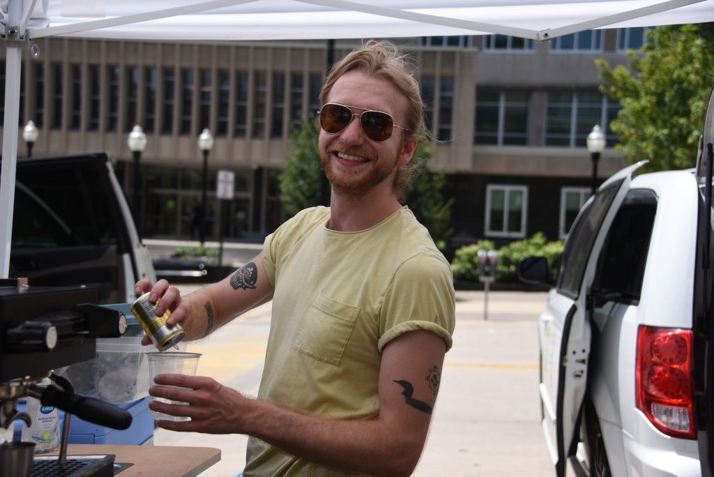 A man in yellow wearing sunglasses pours a tonic water while making a tonic and espresso
