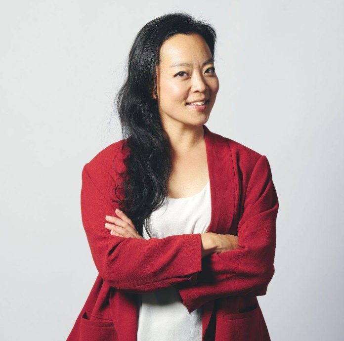 A woman with arms crossed in a red jacket and white shirt