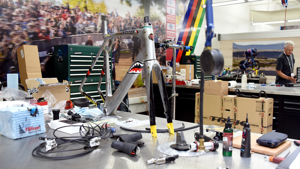 A bike frame with a mouth with sharp teeth painted on it sits on a work desk