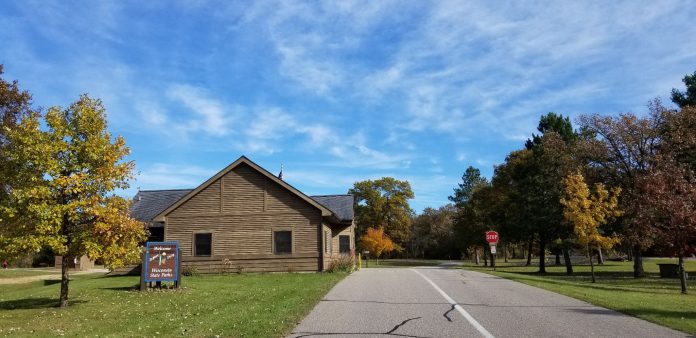 A brown building next to a paved road with trees and a blue sky
