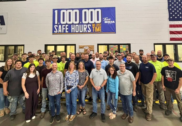 A group at Muza stands for a photo in front of a banner noting one million hours without an injury resulting in loss work time