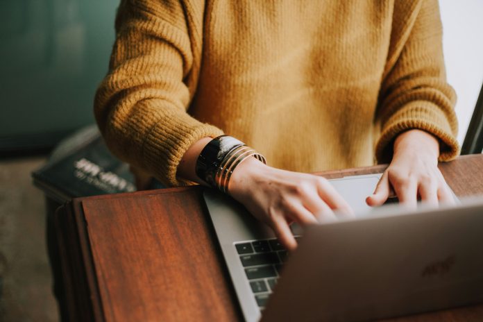 Someone in a mustard-colored sweater typing on a laptop