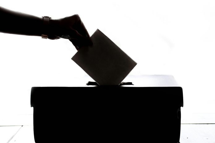 A blackened image of someone dropping a ballot into a box