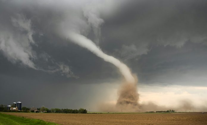 A tornado in a farm field with a farm to the left of it