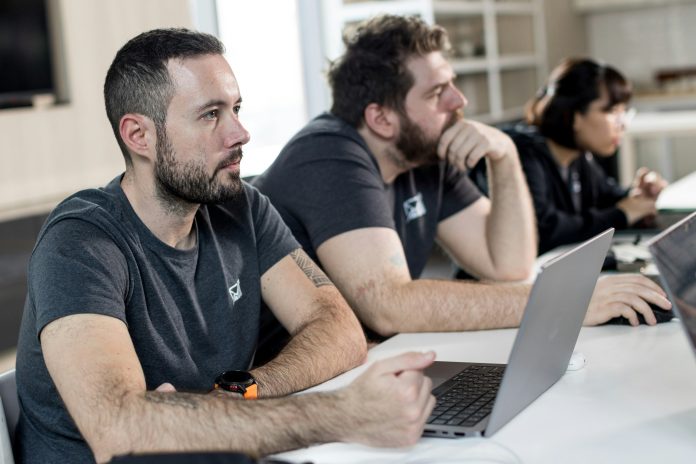 Three people sit at a table with laptops