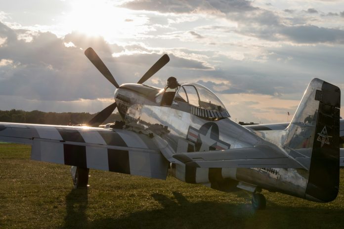 A single-seat silver airplane facing the sun, hiding behind clouds