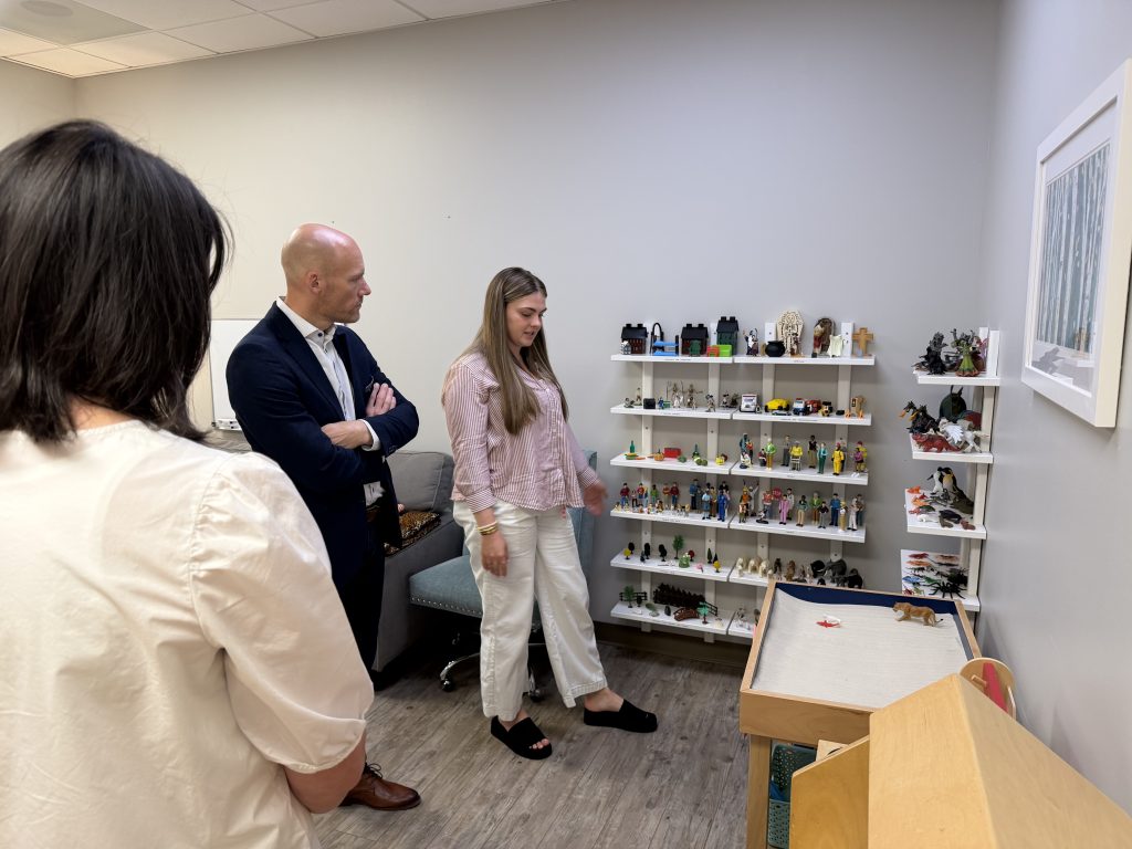 Three people tour a room at the Canopy Center with shoes against a wall on a shelf