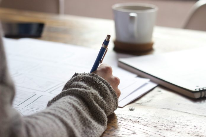 A hand holding a pen while writing on paper