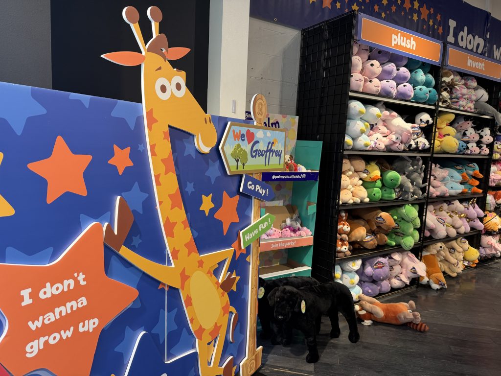 Geoffrey the giraffe by shelves of plushies