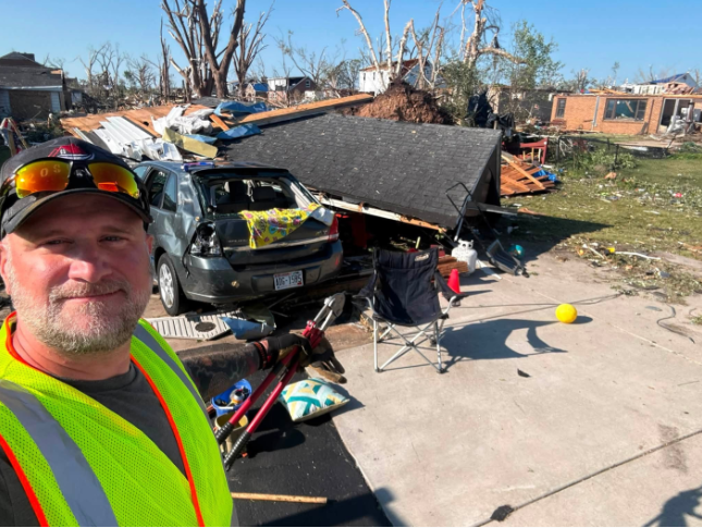 A man taking a selfie with a damaged home
