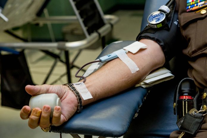An arm with a needle in it with a person giving blood